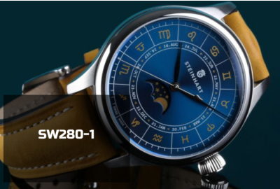 Detailaufnahme des blauen Zifferblatts einer Steinhart-Uhr mit Mondphasenanzeige und astrologischen Symbolen. Die silberfarbenen Zeiger zeigen auf Datums- und Tierkreiszeichen. Ein sichtbares Schweizer Automatikwerk vom Typ SW280-1 treibt die Uhr an.