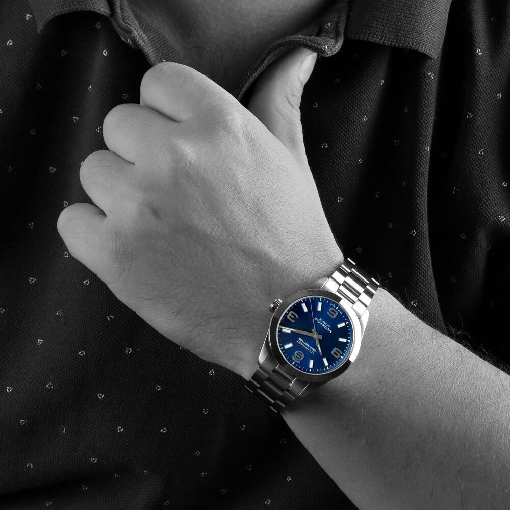 Schwarz-wei&szlig;-Foto eines Handgelenks mit einer silbernen Steinhart Watches Armbanduhr mit blauem Zifferblatt; die Hand greift an den Kragen eines dunklen Poloshirts.